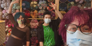 A selfie of three people. Eleanor at the front, she has short purple hair and glasses. Casper, behind, is wearing a green t shirt, he's making a peace sign. Katie on the left is dressed in all black. They’re all wearing masks. 
