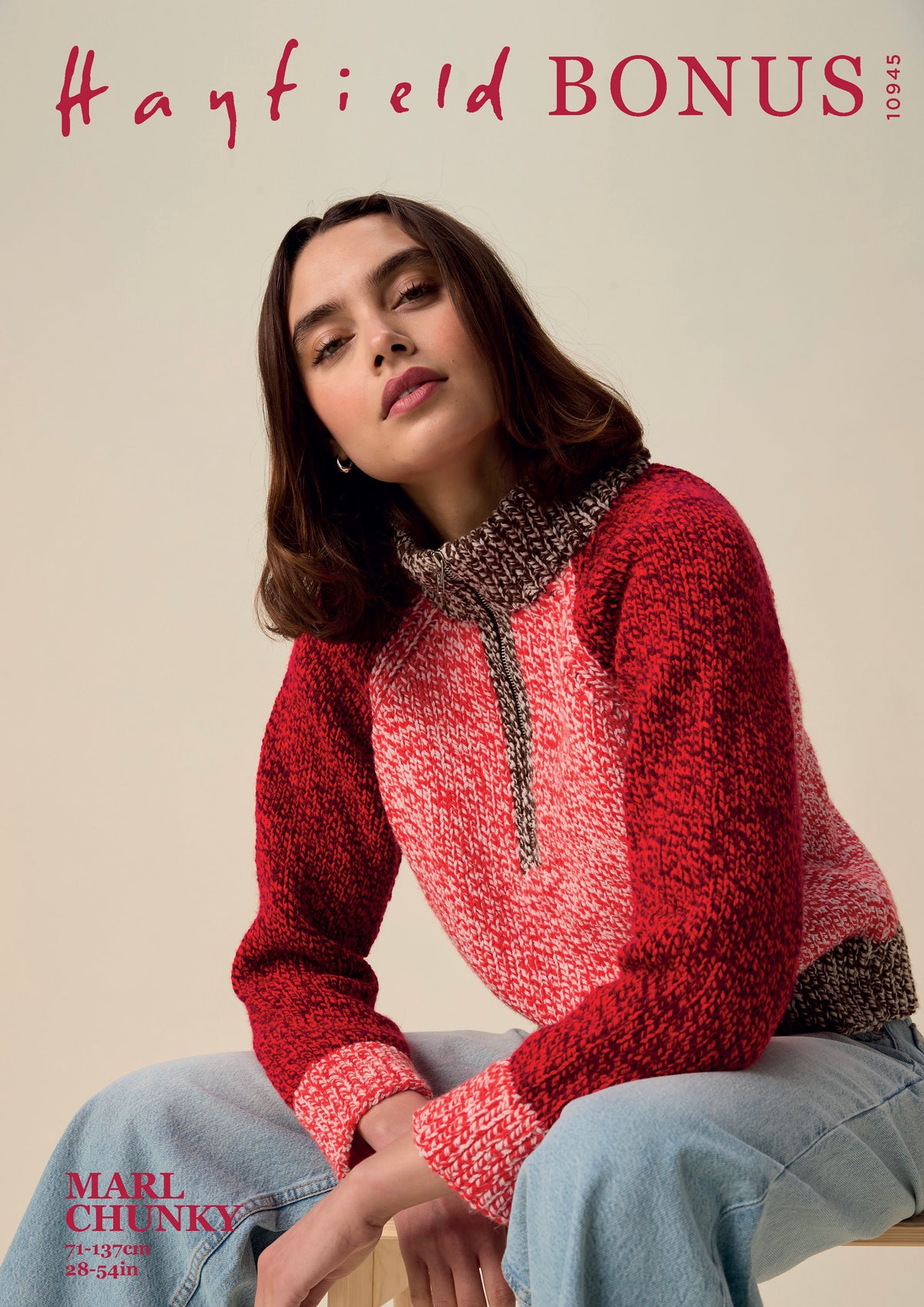 A woman seated against a plain beige studio background wearing a textured knit sweater with a red and pink marled body, a darker brown patterned yoke, and light blue jeans. Large text at the top reads 'Hayfield BONUS' and text at the bottom left reads 'MARL CHUNKY'.